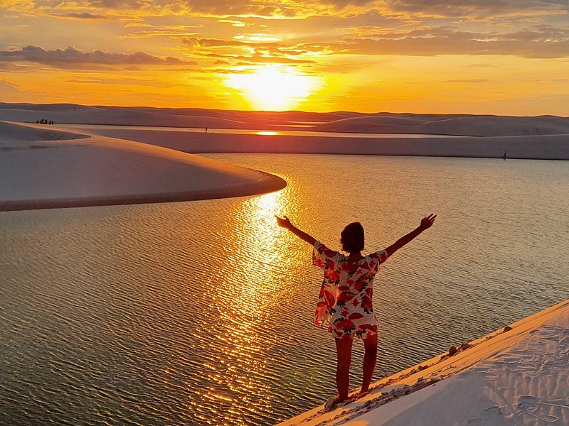 Turista de braços abertos no pôr do sol sobre a lagoa
